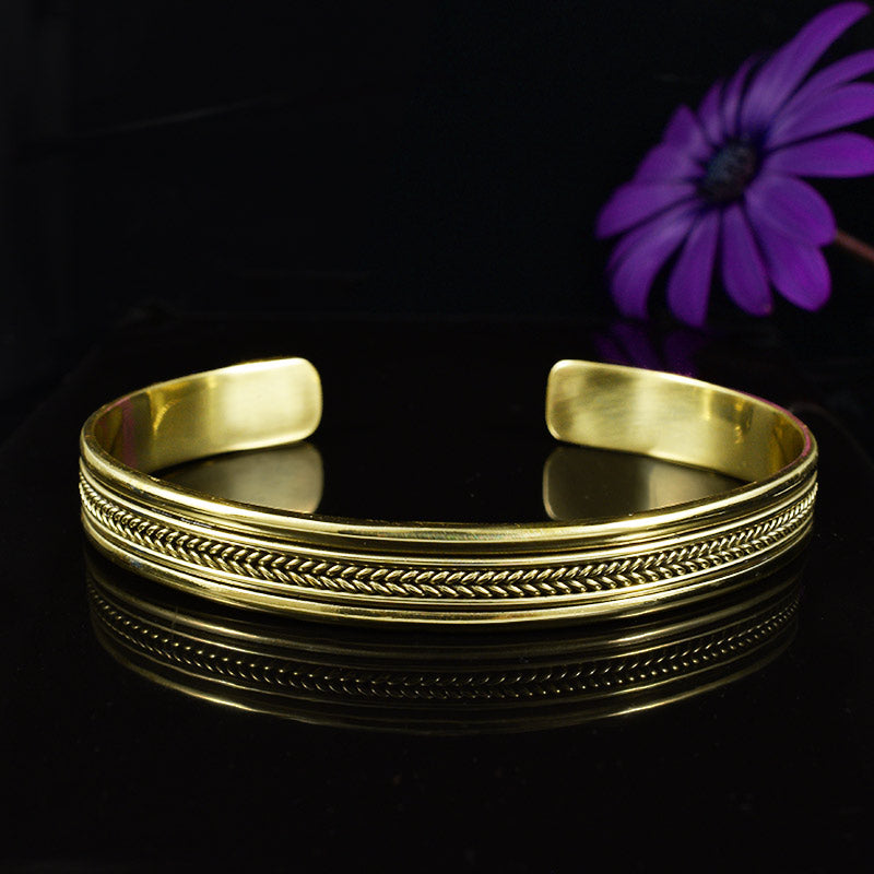 a brass cuff bangle on a black background with a purple flower