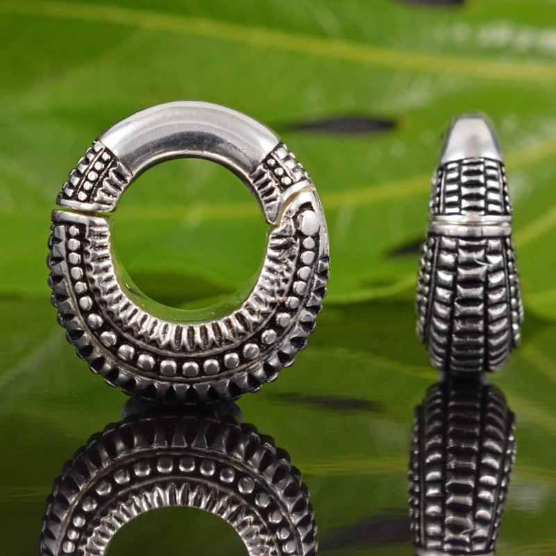 silver hinged ear weight on a reflective green background