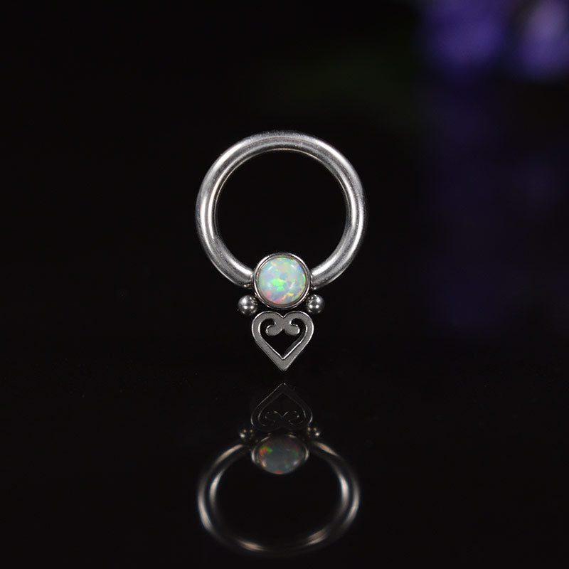 a small ball closure ring BCR with an opal stone and a heart decoration on a black background