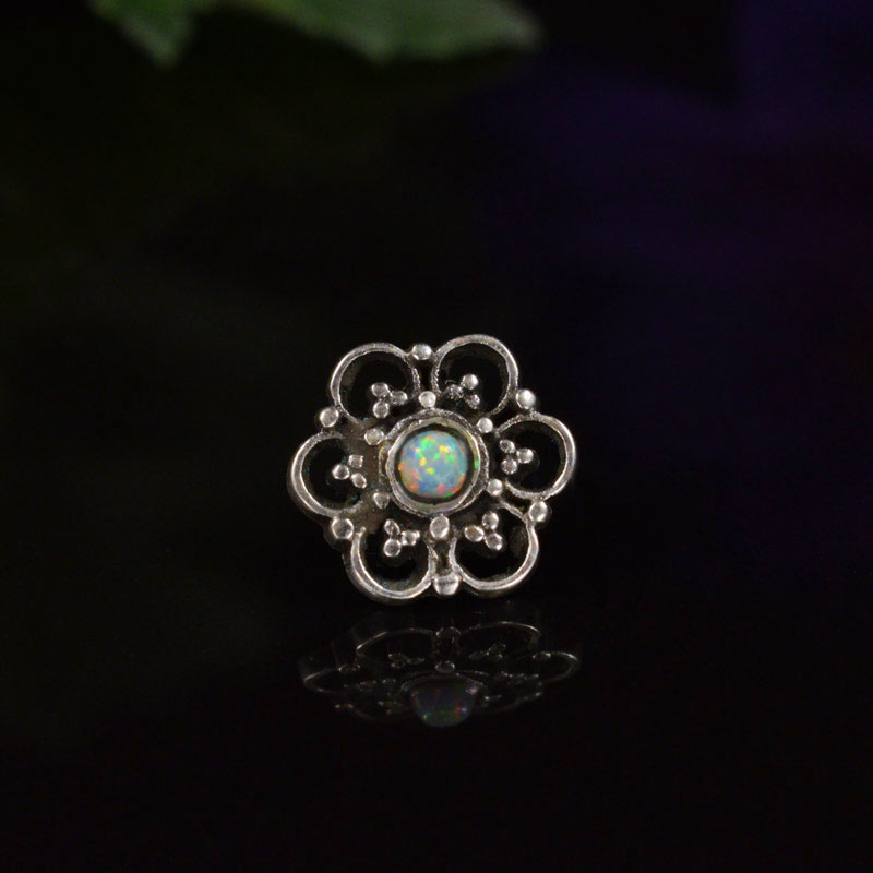 A tribal style threadless piercing end with an opal stone on a black background
