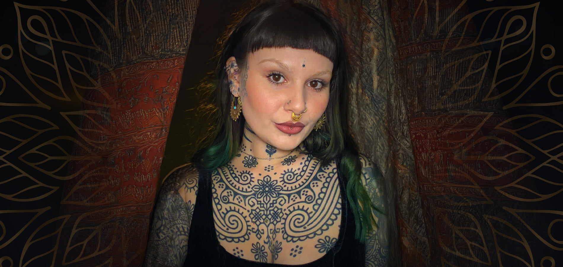 bohemian woman with tattoos, tribal earrings and piercings standing in front of Indian drapes