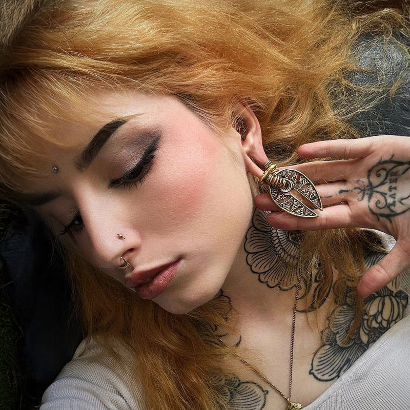 alternative woman with tattoos wearing labret piercings, nose stud clicker rings and tribal earrings lying on mossy ground
