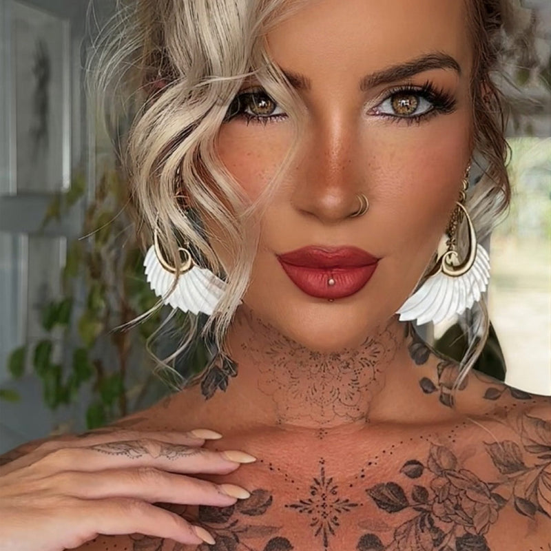 boho woman with tattoos and piercings wearing mother of pearl wing earrings