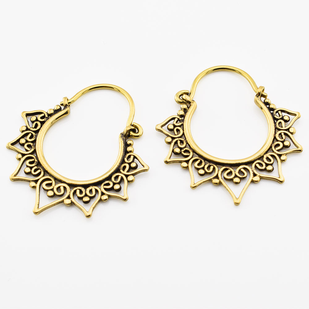 A pair of golden brass tribal hoop earrings with intricate heart filigree cutouts and decorative pointed tips, displayed on a clean white background.