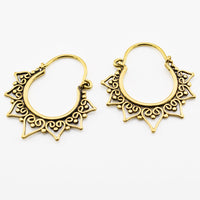 A pair of golden brass tribal hoop earrings with intricate heart filigree cutouts and decorative pointed tips, displayed on a clean white background.