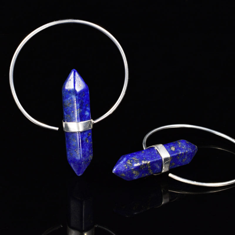 Two silver plated hoop earrings with faceted blue lapis lazuli crystal point pendants, displayed on a reflective black surface.