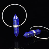 Two silver plated hoop earrings with faceted blue lapis lazuli crystal point pendants, displayed on a reflective black surface.