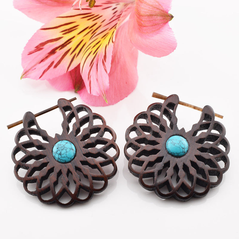 Wooden floral earrings with turquoise stone centers on a white background with a pink flower.