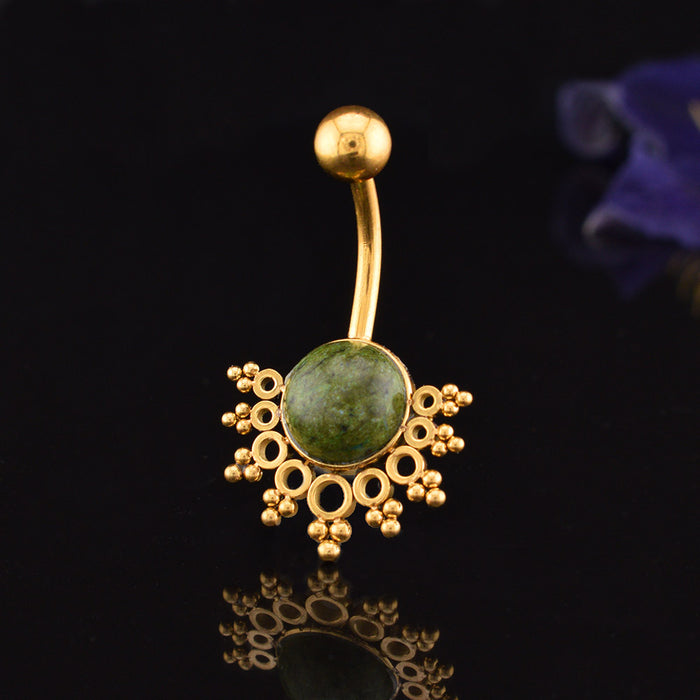 Gold-plated curved barbell belly button ring with a round green african jade stone centerpiece and ornate filigree details, shown on a reflective black background.