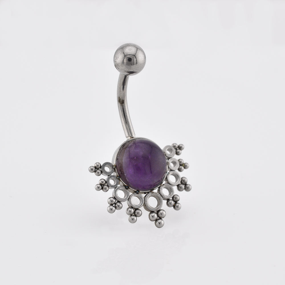 A tribal navel bar/ curved barbell belly button ring featuring a central purple amethyst gemstone surrounded by a decorative snowflake-like cluster of small silver beads and loops, shown on a plain light gray background.