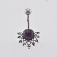 A navel piercing bar featuring a round purple amethyst in the center, surrounded by an intricate openwork silver filigree design, on a plain light gray background.