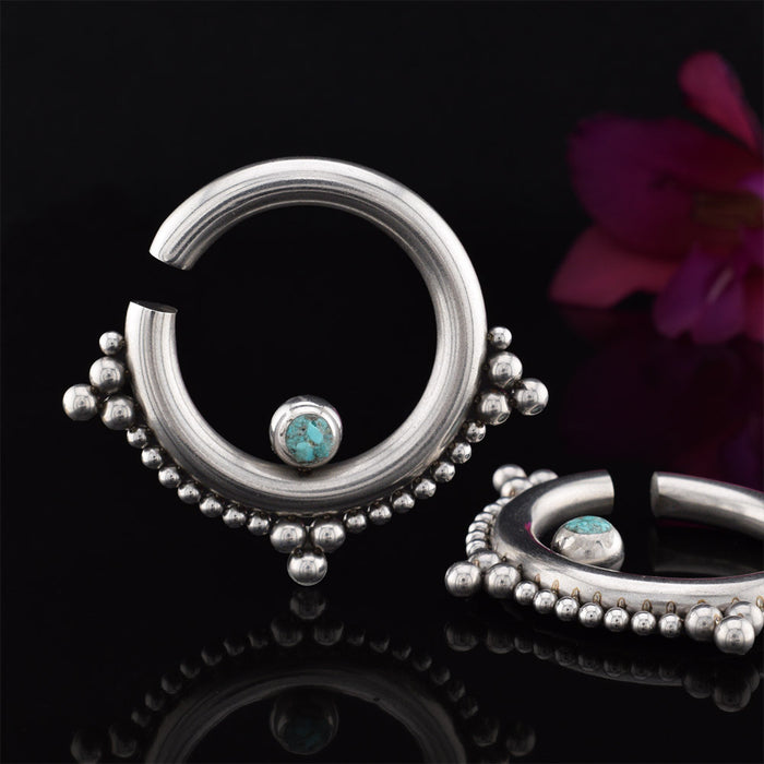 Ear hangers in steel with tribal beading and turquoise stone on a black reflective surface with a flower in the background