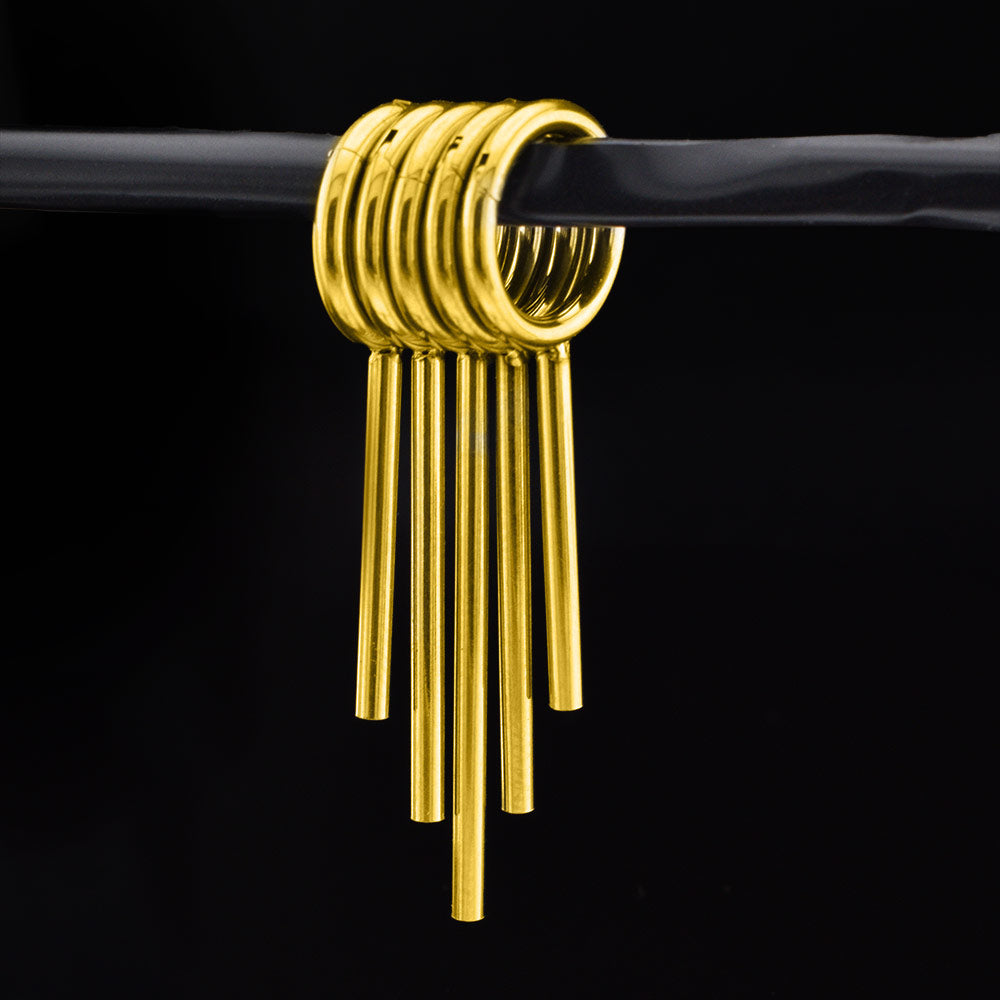 Set of 5 gold coloured clicker rings with drop spikes for wearing in stretched ears on a black background 