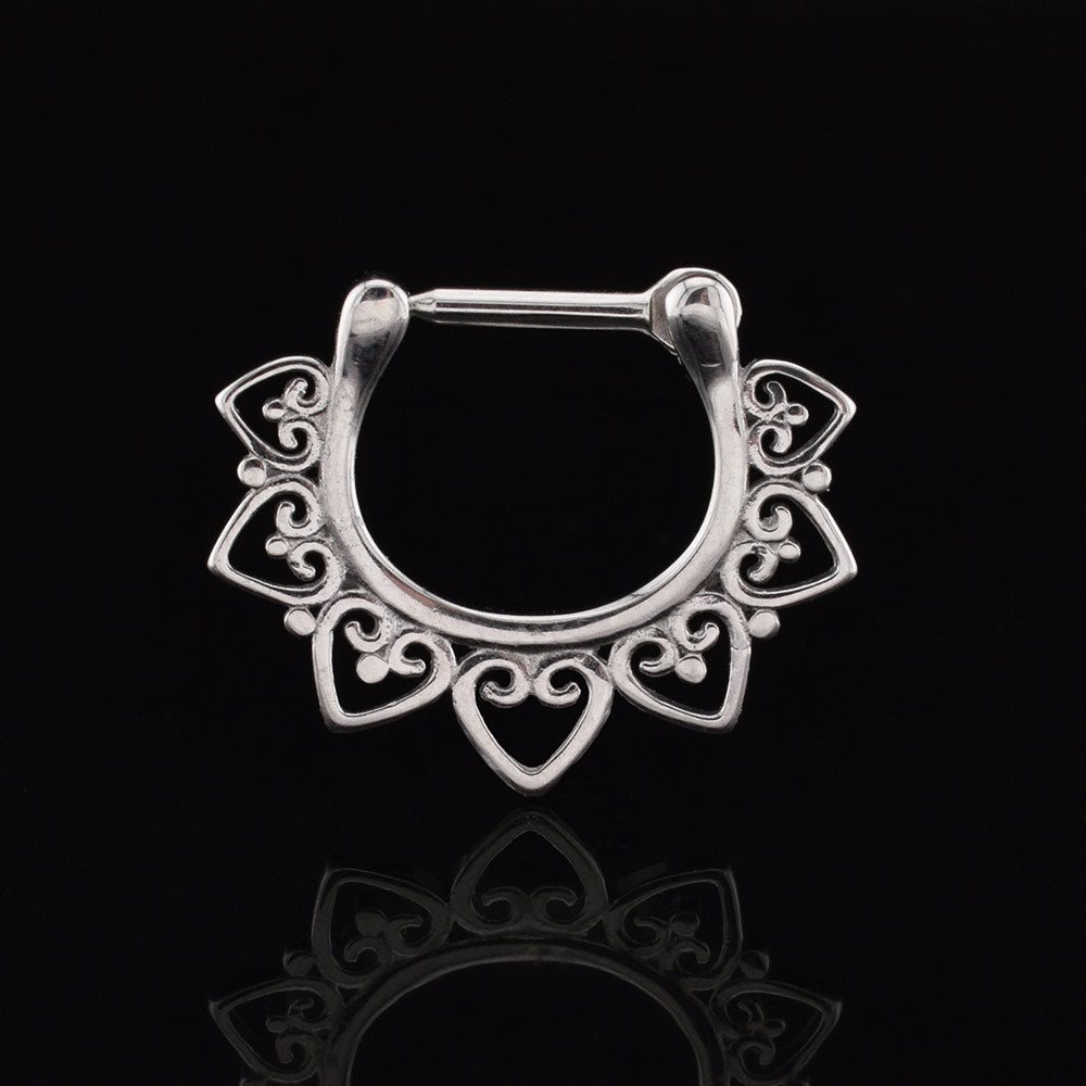 A septum clicker ring with a heart filigree design on a black reflective background