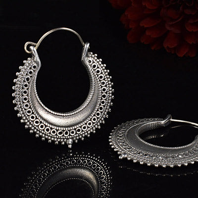silver hoop earrings in a tribal indian design on a black reflective background