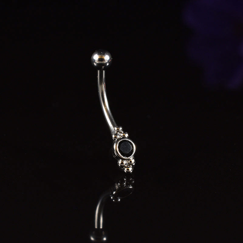 A curved barbell with triple beads and black stones shown on a reflective black background.