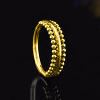 A gold steel hinged segment ring with a double row of small, polished bead-like details, shown on a reflective black background.