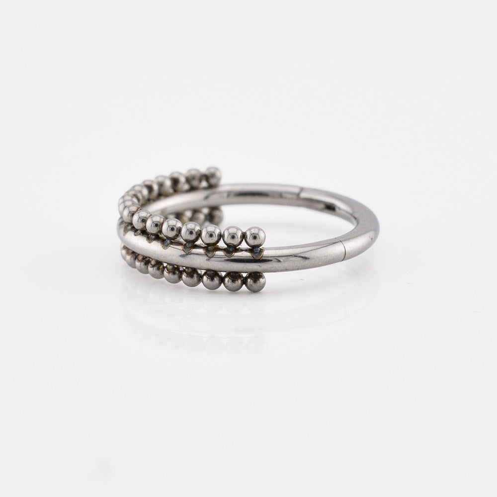 A surgical steel triple-band hinged segment clicker ring featuring one smooth band and two beaded bands, displayed on a reflective white surface.