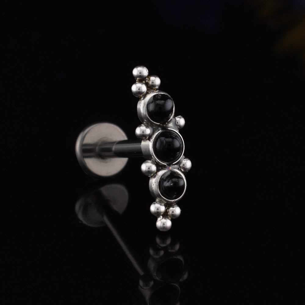 Helix Labret Earring with a cascade of three black onyx stones decorated with tribal beading in surgical steel on a black relective background