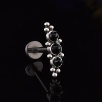 Helix Labret Earring with a cascade of three black onyx stones decorated with tribal beading in surgical steel on a black relective background