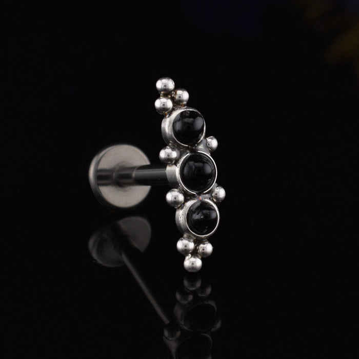 Helix Labret Earring with a cascade of three black onyx stones decorated with tribal beading in surgical steel on a black relective background