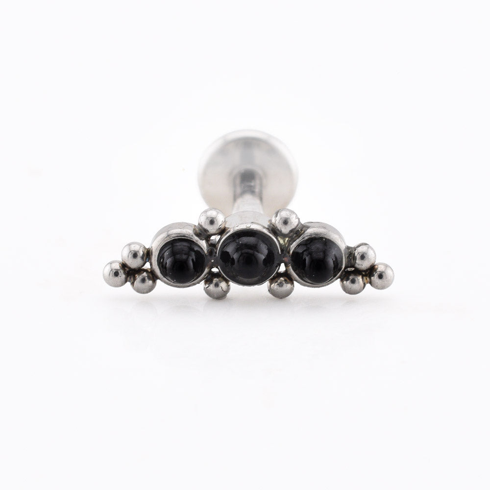 A silver-toned body jewelry piece, likely a labret or piercing stud, featuring three round black gemstones in a row with small metallic beads on each side, set against a plain white background.