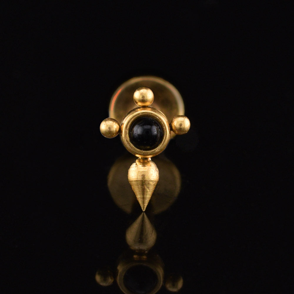 Labret earring in gold steel with a tuareg inspired cross design centred with a black onyx stone on a black reflective backgound