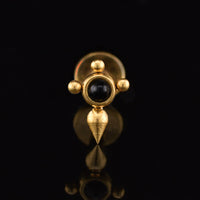 Labret earring in gold steel with a tuareg inspired cross design centred with a black onyx stone on a black reflective backgound