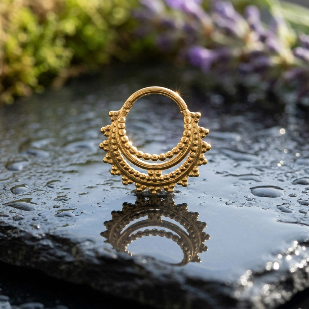 Gold clicker ring in a tribal indian design on a wet stone surface with blurred floral background