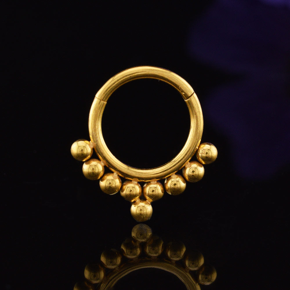 clicker ring in gold steel with a tribal beads design on a black reflective surface