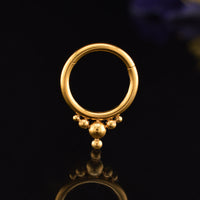 A gold  steel hoop hinged segment piercing ring with a fixed tribal beaded fringe, displayed on a reflective black surface.