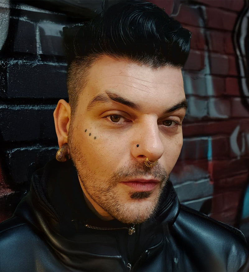 alternative man wearing ear weights and septum piercing and nose stud leaning against a wall with graffiti