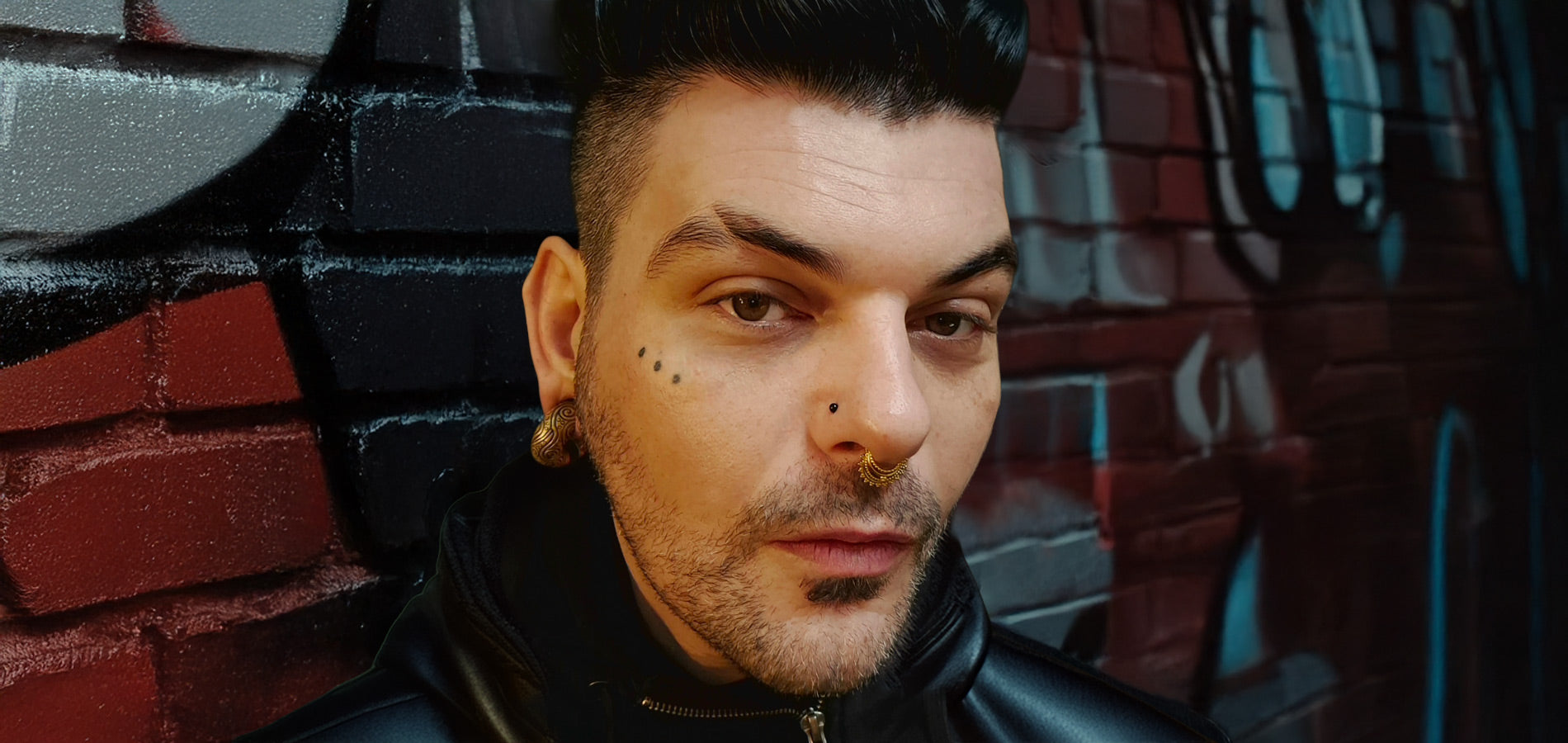 alternative man wearing ear weights and septum piercing and nose stud leaning against a wall with graffiti