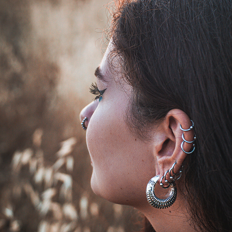 a woman looking away with multiple helix earrings and an ear weight in her ear.